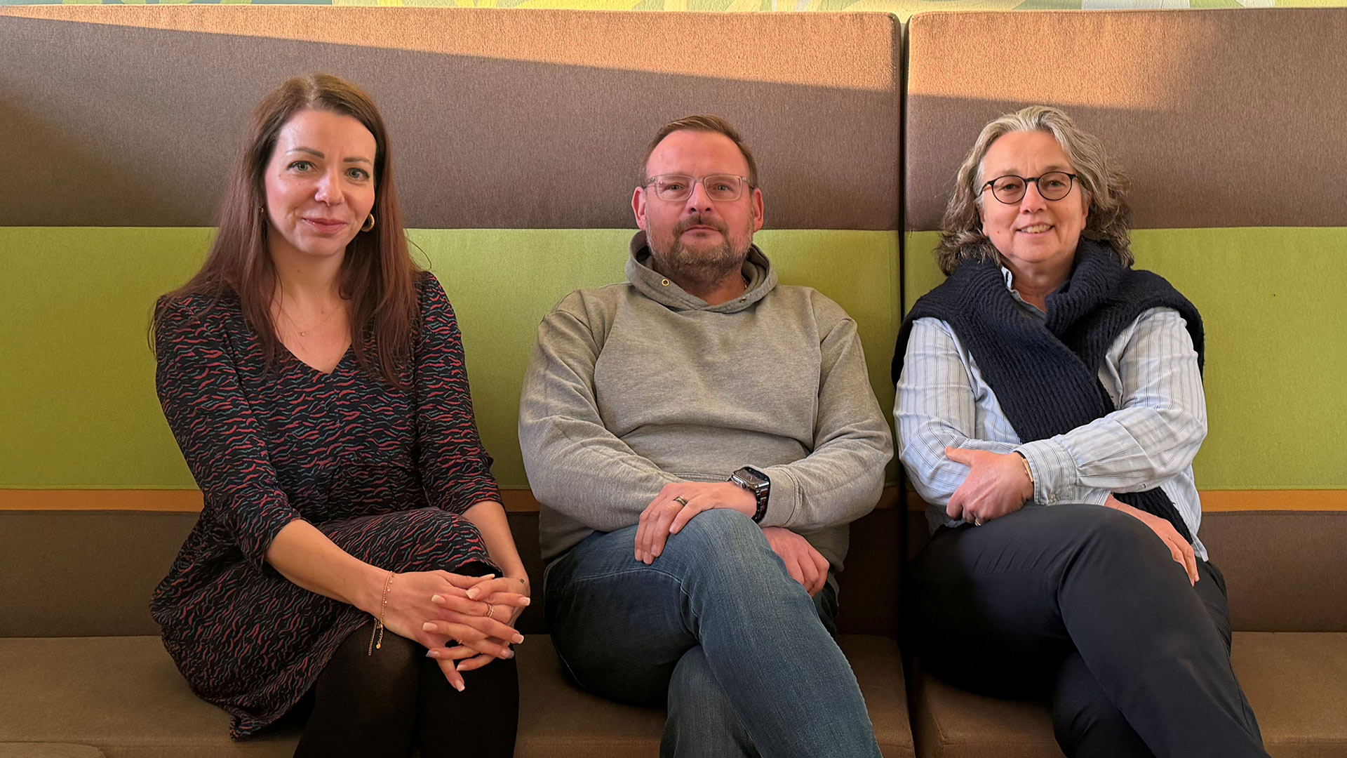 Drei Personen sitzen nebeneinander auf einem Sofa